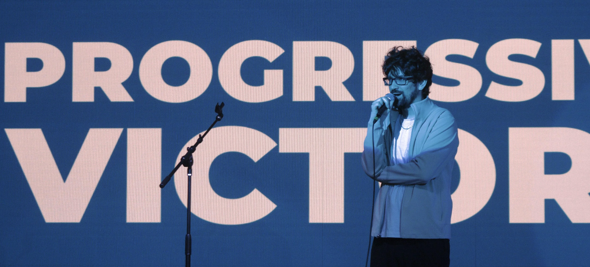 Colorized photo showing Steven standing on stage with text reading 'PROGRESSIVE VICTORY' in the background